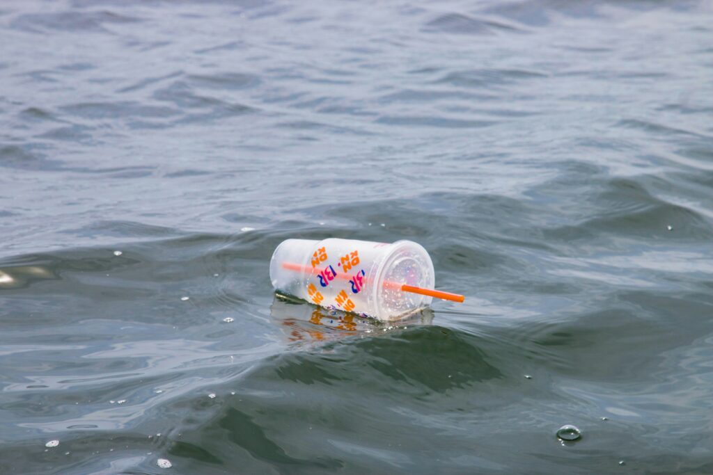 A clear plastic cup and straw float in a body of water.