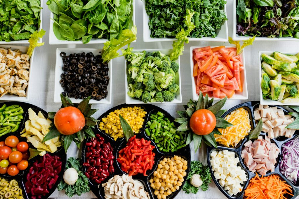 A horizontal array of vegetables and salad ingredients on back and white plates on a white table.