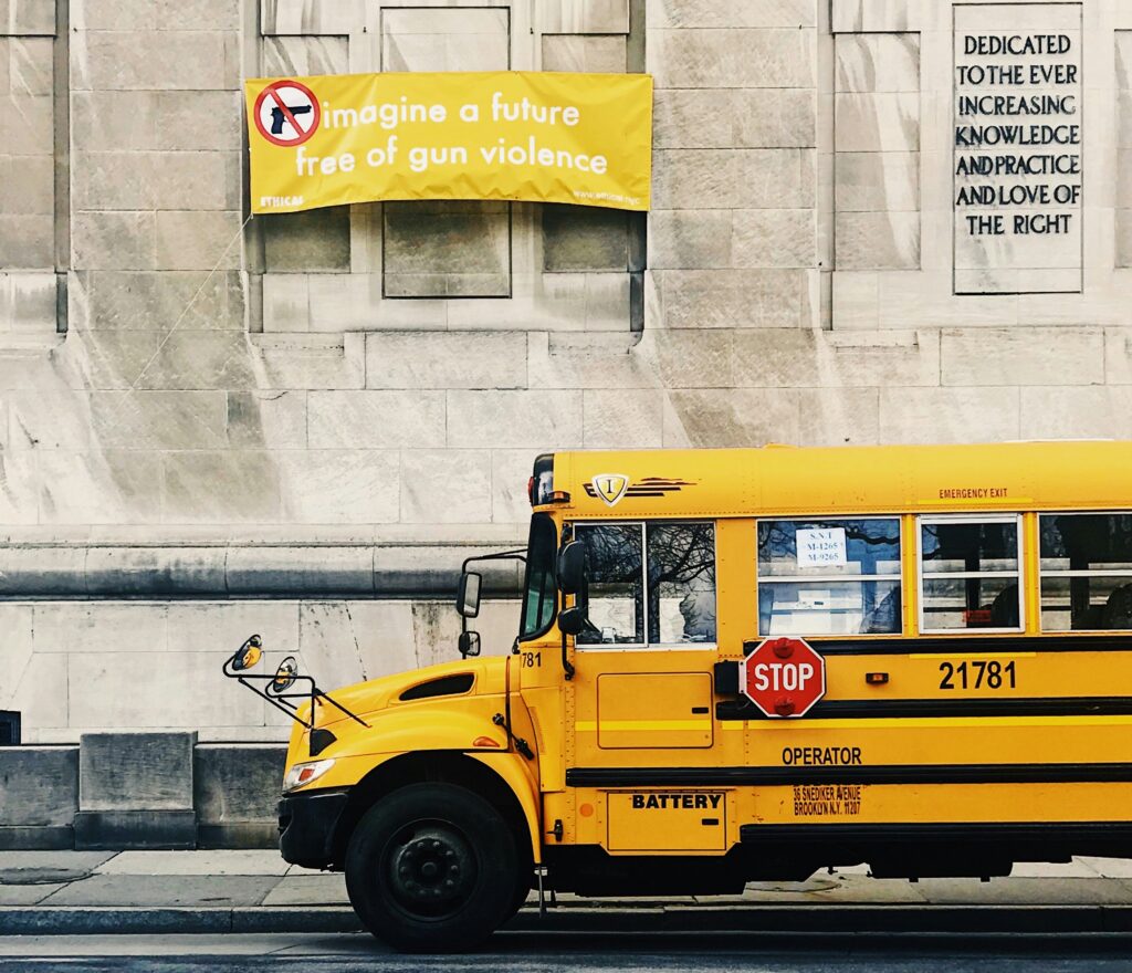 A yellow sign against gun violence appears on a stone wall above a yellow school bus.